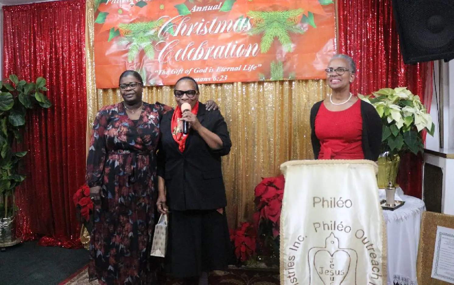 Three women posing at a Christmas celebration event with festive decorations.