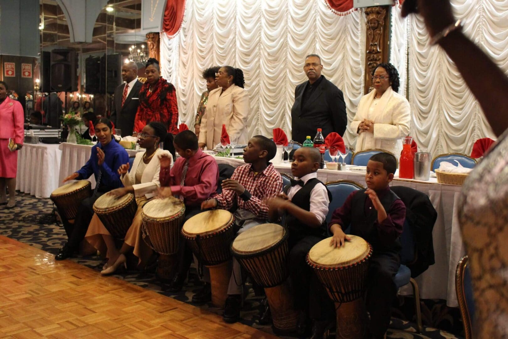 Group playing traditional African drums indoors, dressed in colorful attire.