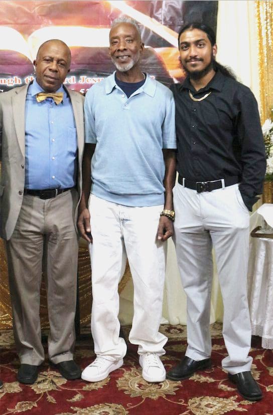 Three men posing indoors, dressed in casual to formal attire.